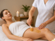 Esteticista aplicando cera de depilação quente na coxa de uma cliente em uma maca de spa, com luz suave e velas.
